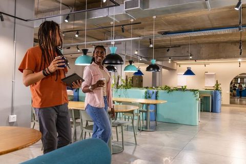 Colleagues walking through modern coworking lounge holding tablet and coffee cups