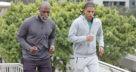 Older black man and young multiracial man jogging up urban stairs for fitness