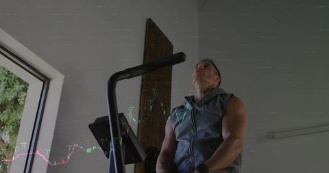 Muscular man doing intense cardio on elliptical in home garage gym with sleeveless hoodie