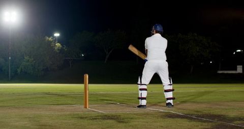 Night cricket batsman standing at crease under floodlights preparing to face delivery