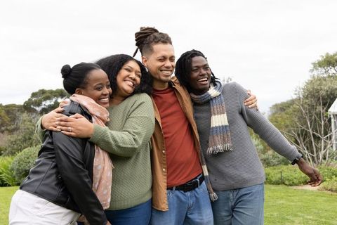 Friends hugging and laughing on park lawn wearing scarves and sweaters
