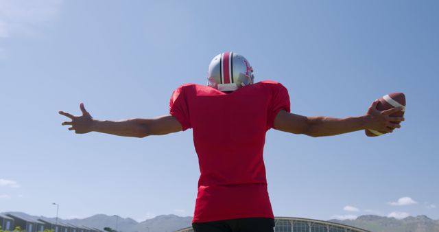Football player standing outdoors with outstretched arms celebrating a touchdown. Use this for sports marketing, team victory promotions, or illustrating enthusiasm in outdoor sports.