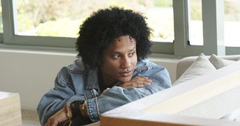 Contemplating mid-adult african american man leaning on sofa, sunlit living room, denim jacket