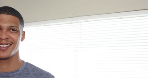 African american man smiling by window blinds with backlight and ample copy space