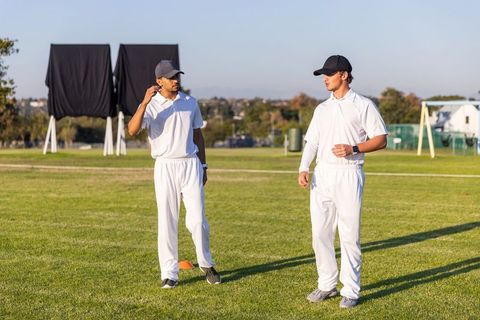 Two male cricketers wearing white kit standing on suburban grass field during training