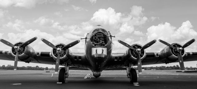 A historic World War II bomber aircraft with four propellers, parked on a runway under a cloudy sky. Ideal for use in articles or presentations about military history and aviation, vintage aircraft enthusiasts, and wartime memorabilia collectors.