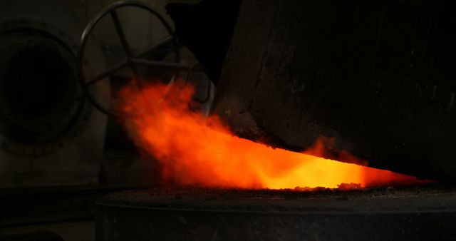 Molten metal pouring out of a furnace in an industrial foundry, showcasing the intense heat and vibrant orange glow. This is typically found in metalworking and manufacturing industries. Ideal for use in materials focused on heavy industry, manufacturing processes, construction materials, and metallurgy.