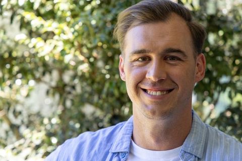 Smiling man posing in sunlit garden wearing light blue shirt over white t-shirt headshot