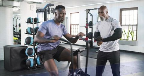 Intense air bike interval training with coach timing high-energy workout in bright modern gym
