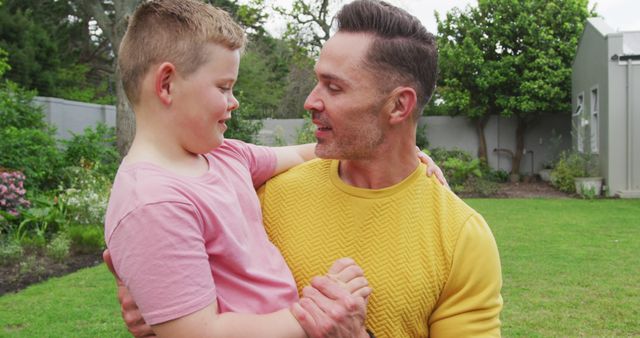 Father holding his son in backyard garden leads to happy and affectionate moment. Suitable for parenting articles, family lifestyle blogs, Father's Day promotions and advertisements focusing on family activities.