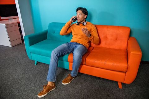 Man talking on phone and gesturing on two-tone sofa in modern office lounge with headphones