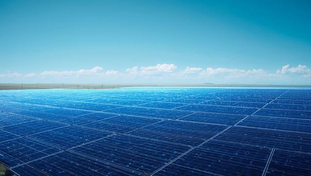 Expansive ground-mounted solar farm stretching across rural plain under clear blue sky