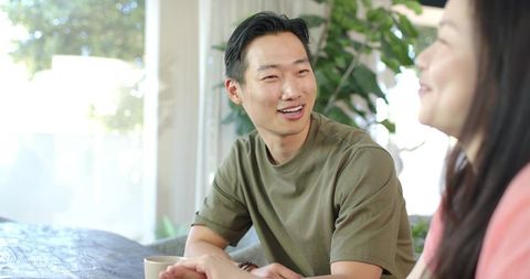 Diverse couple sharing relaxed morning conversation at sunlit dining table with mug