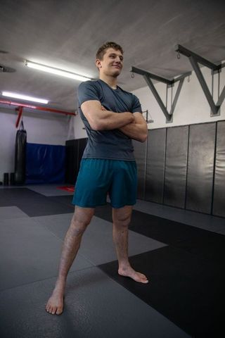 Confident young athlete standing barefoot with arms crossed in martial arts gym