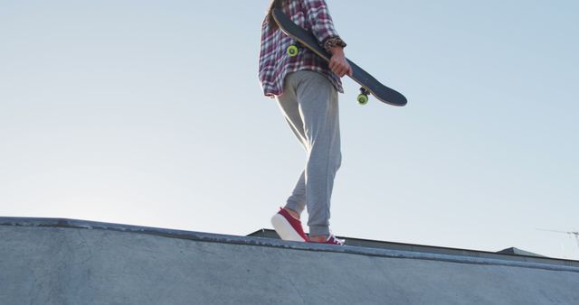 Low section of caucasian woman holding skateboard, walking on sunny day. hanging out at skatepark in summer.