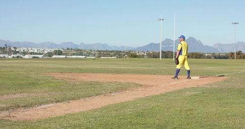 Baseball player standing on base in yellow uniform on suburban field with mountain backdrop