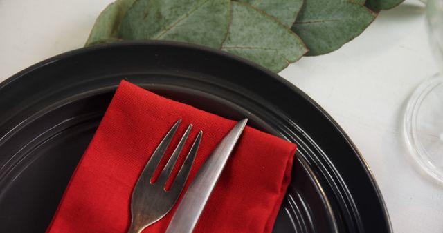A black plate with a red napkin and a fork on top, with copy space. The setting suggests a simple yet elegant dining arrangement, ready for a meal.
