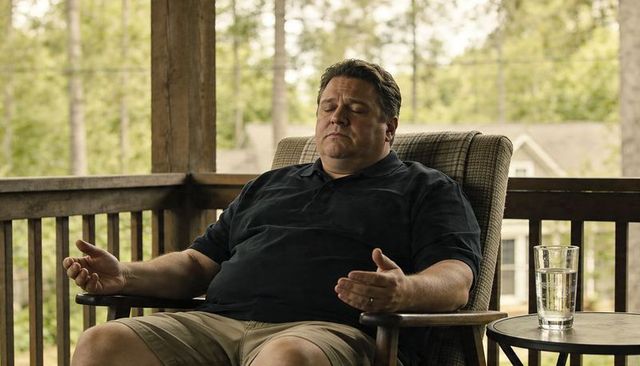 Man relaxing on porch chair with closed eyes and glass of water on side table on suburban deck