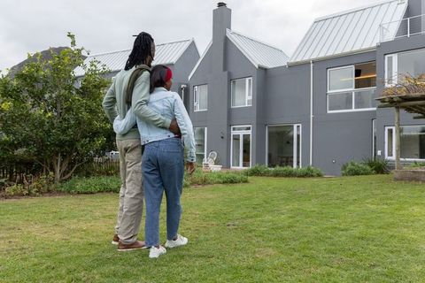 African american couple embracing and admiring modern gray house with garden and balcony
