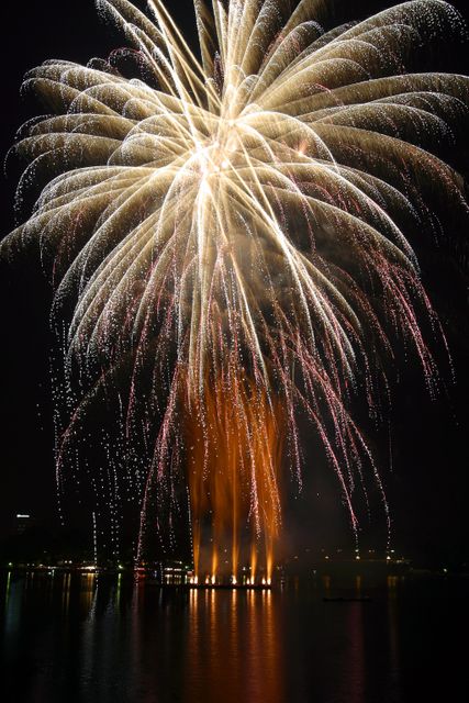 Bright, colorful fireworks exploding in night sky, reflecting on tranquil water. Useful for backgrounds, holiday promotions, event advertisements, or festive greetings.