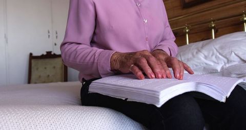 Senior Woman Reading Braille Book on Bedroom Bedside
