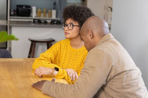 Couple discussing plans at kitchen table while woman checking smartwatch