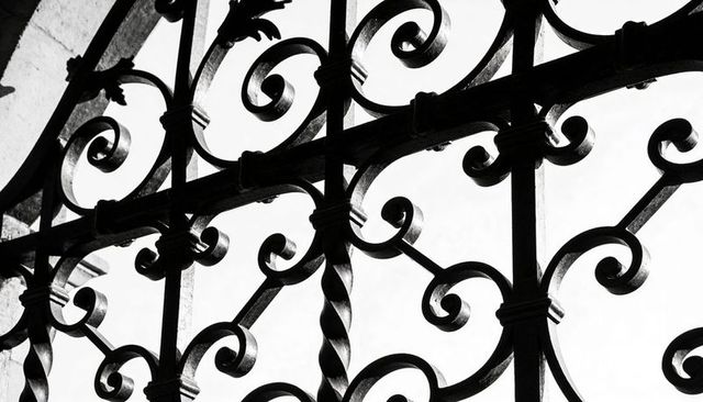 Wrought-iron scrollwork casting silhouettes against stone arch