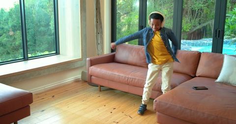 African american boy dancing with headphones in modern living room by pool