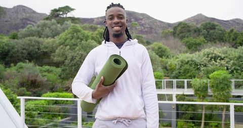 Smiling African American Man Holding Rolled Yoga Mat on Rooftop Deck for Outdoor Fitness, Wellness