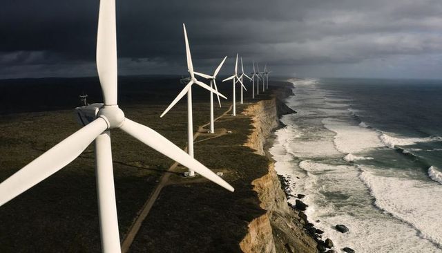 Coastal wind farm stretching along rugged cliffs with powerful surf and stormy sky