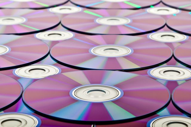 Close-up view of stacked compact discs creating a seamless pattern with reflective surfaces. Smooth metallic surface with a spectrum of colors highlighting detail and design. Ideal for technology backgrounds, digital media promotions, and articles on data storage or the evolution of music formats.