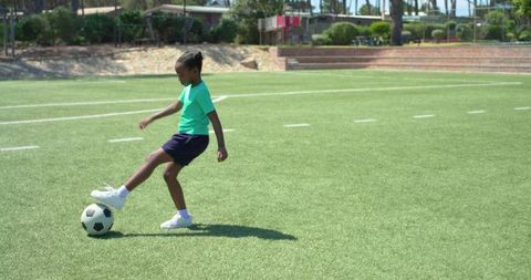 Youth player balancing on soccer ball and preparing to kick on green turf in sunny field