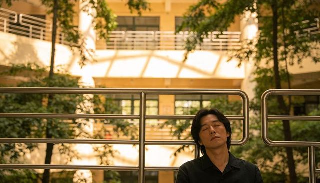 Man resting head on stainless-steel railing in sunlit atrium, serene contemplative moment