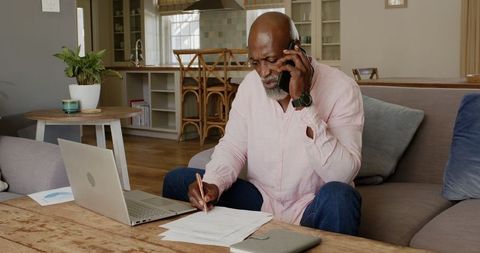 Remote businessman on call while writing job notes at home