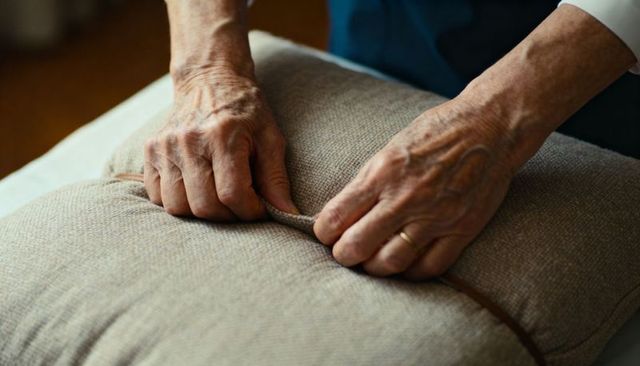 Senior hands adjusting beige cushion piping with gold wedding band close-up for home care