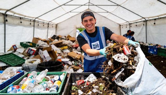 Smiling volunteer sorting compost and recycling under tent, emptying sack into bin