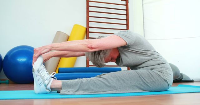 Elderly woman touching her toes on exercise mat at the rehabilitation center 