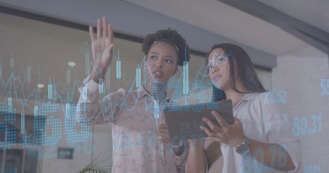 Businesswomen analyzing digital financial graphs in modern office
