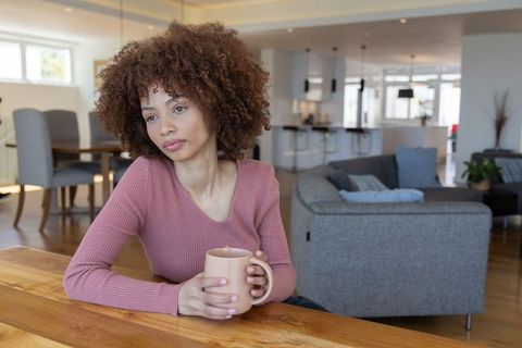 African american woman holding mug gazing thoughtfully in modern open-plan living room