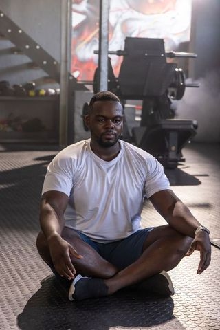 African american athlete sitting cross-legged in gym wearing white tee and smartwatch