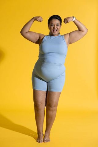 Confident plus-size woman flexing muscles wearing blue activewear on vibrant yellow