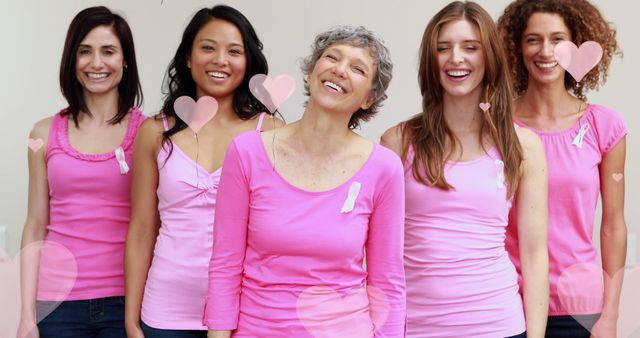 Image of pink hearts floating over diverse group of smiling women in pink with cancer ribbons on. breast cancer positive female health awareness campaign concept digitally generated image.