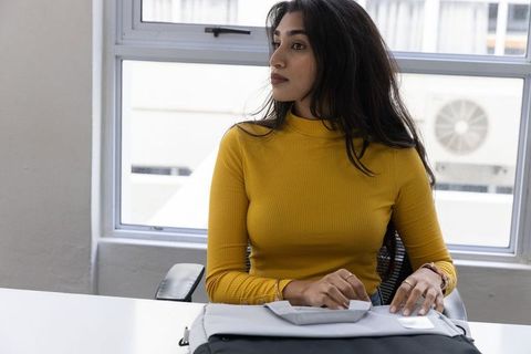 Indian professional woman wearing mustard ribbed top looking out window in modern office