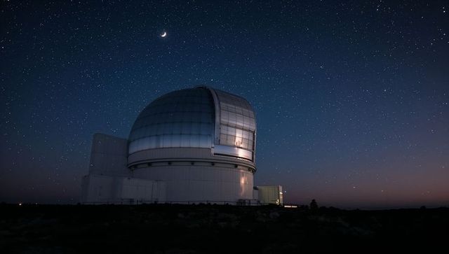 Observatory under starlit sky with crescent moon at dusk