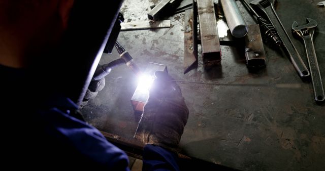 Worker operating blow torch in a workshop setting, wearing protective gloves. Ideal for illustrating manual labor, skilled trades, industrial safety, and metalworking processes in manufacturing or engineering. Can be used in articles, advertisements or educational materials related to welding, craftsmanship, and industrial safety.