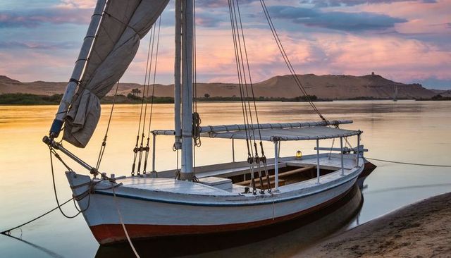 Resting wooden sailboat at pastel sunset on calm river with lantern glow and reflections