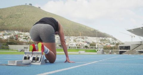Sprinter preparing at starting blocks on blue track with neon running spikes