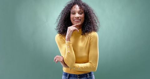 Confident african american woman smiling, posing in mustard sweater on green backdrop