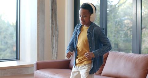 Young boy dancing with wireless headphones in bright modern living room