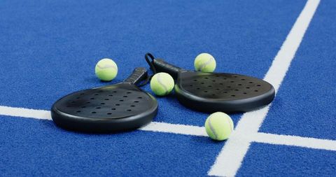 Black padel rackets on blue court with tennis balls
